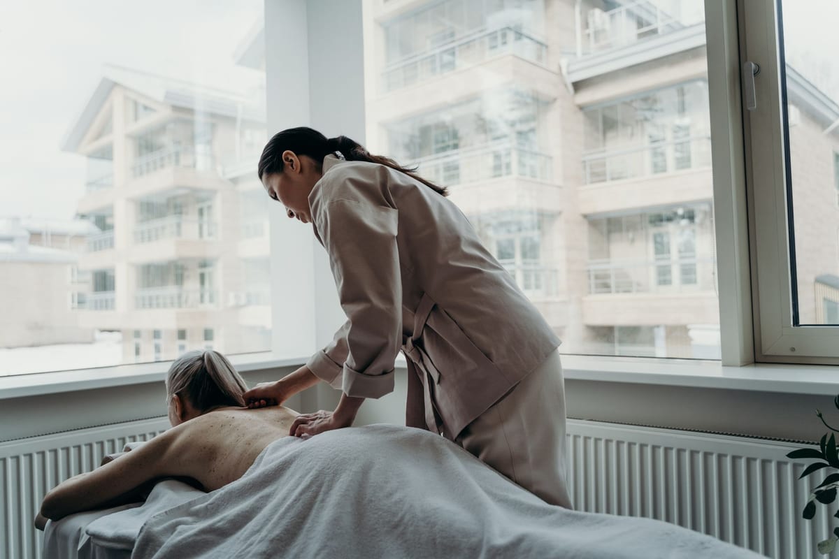 A registered massage therapist working on a patient's back beside a bright window