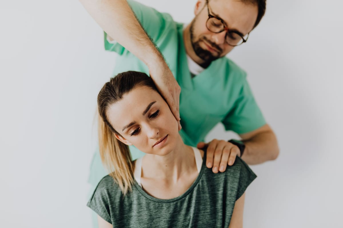 A clinician performing a hands-on neck assessment on a seated patient